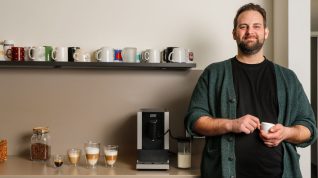 Kleiner Kaffeevollautomat und Redakteur mit Tasse in der Hand